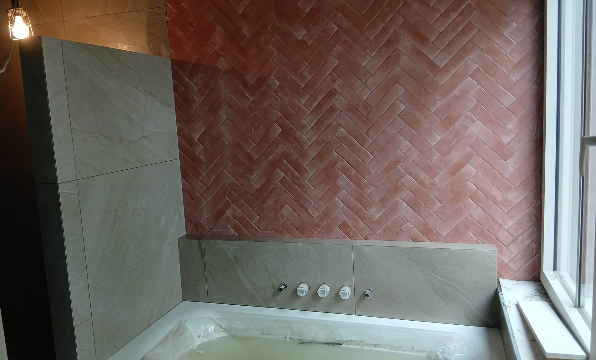 Terracotta handvormtegels in visgraatverband boven een bad