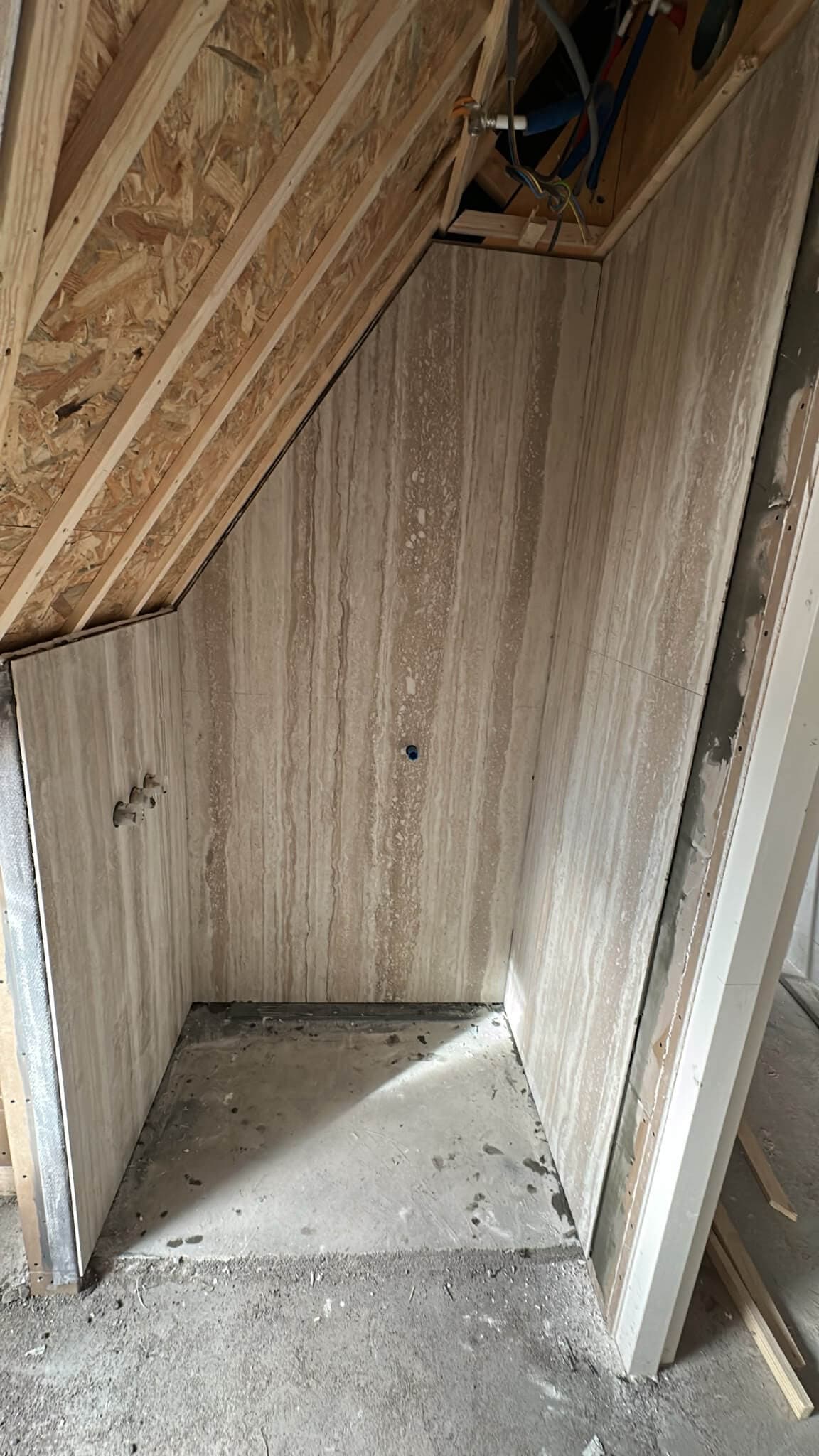 Doucheruimte onder een schuin dak bekleed met travertinlook slabs